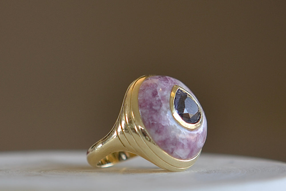 The Small or petite Lollipop Ring in Trolleite and Spinel by Retrouvai is a one of a kind signet ring featuring a chunky and rounded stone face with a translucent center stone set on a tiered edge and tapered band. This one is purple trolleite and a pear cut spinel in the center.  