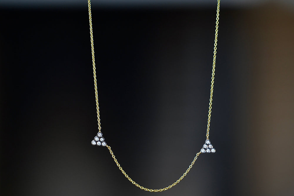 Duo triangle necklace by Yannis Sergakis is made out of two triangles of six bezel set and rhodium plated round cut diamonds each hang slightly asymmetrically on an 18k gold chain. 