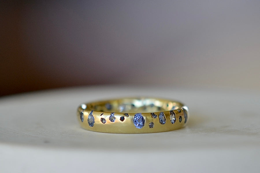 The Cornflower Blue Sapphire Confetti Band designed by Polly Wales is a narrow 18k yellow recycled gold wedding band/ring with speckled ombre light blue sapphires around the circumference. It is cast not set and handmade in Los Angeles.