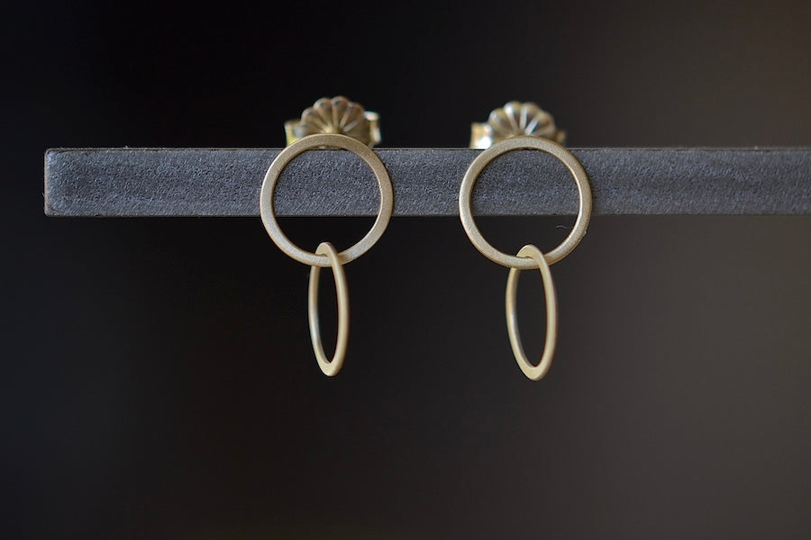 Double Circle Stud Earrings by Carla Caruso are Two thin and flat interlocked circles in 14k yellow gold and satin finish with post closure.