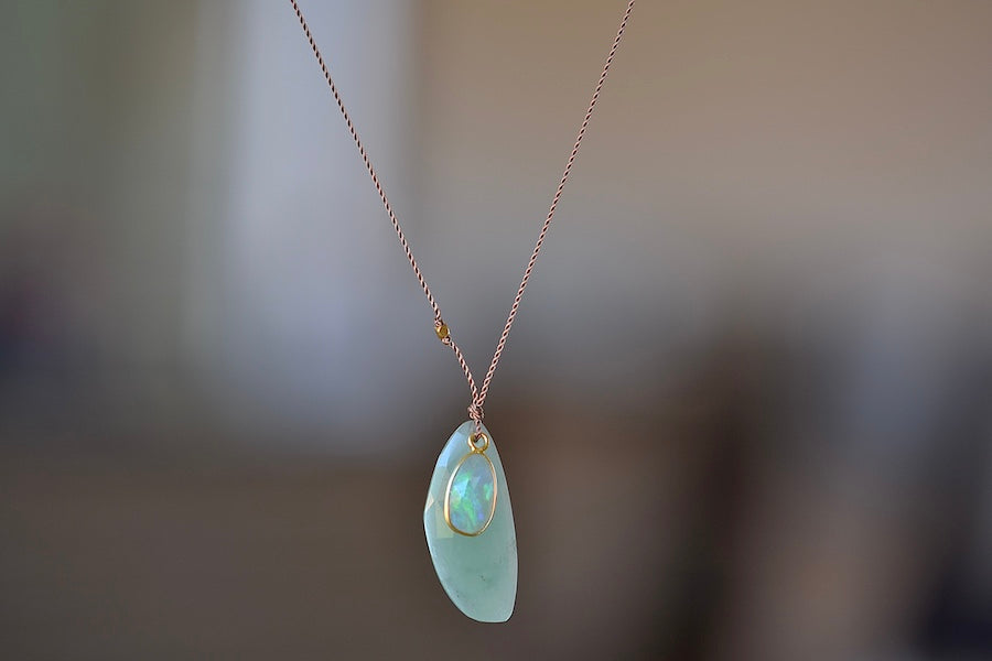 Two Individual stone slices, a larger pale, light green and lightly faceted Green Chalcedony and a smaller multicolored and iridescent opal. The the smaller is set in 18k yellow gold and the piece is accented with a gold bead on the poly nylon string to form this one of a kind organic pendant necklace. 