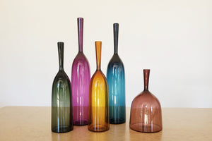 Angelic Bottles by Joe Cariati are mouth blown  Freeblown by glass master Joe Cariati in his Southern California studio, these bottle-form vases evoke the more mass produced mid-century ones that inspired them, large steel blue, small amber orange and wide ultra violet purple.