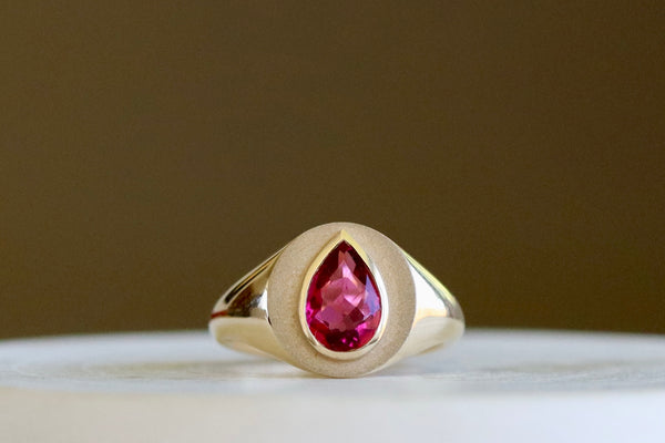 Circle Signet with Pear Tourmaline by Elizabeth Street Jewelry is a multi finish classic circle signet ring with a bezel set rubellite pear tourmaline on a tapered 14k yellow gold band. Handmade in Los Angeles. Size 7.