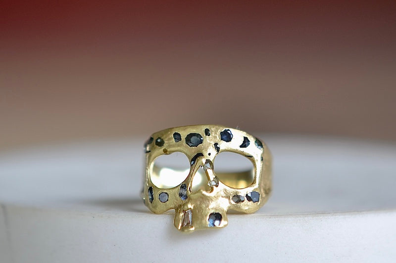 Stoned Mini Snaggle Tooth Skull ring by Polly Wales with green sapphires and a baguette diamond snaggle tooth.