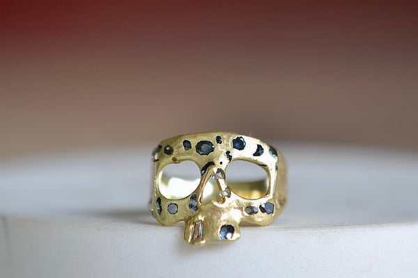 Stoned Mini Snaggle Tooth Skull ring by Polly Wales with green sapphires and a baguette diamond snaggle tooth.