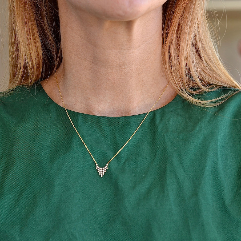 Wearing the Charnières Pétale Pendant Necklace by Yannis Sergakis is twenty-Five (25) rhodium plated round cut diamonds that form a triangular pendant on an 18k gold chain.