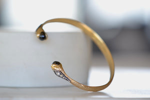
            
                Load image into Gallery viewer, Duo Snake Cuff by Arman Sarkisyan is A single piece of gold is shaped and hammered into a cuff that has snake heads on each end with oxidized silver and diamond detail on each snake and holding a black diamond brio 2.41TCW..
            
        
