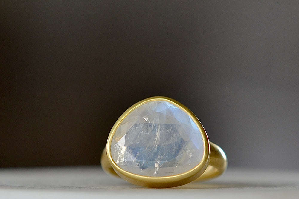 Rainbow Moonstone Greek Ring is designed by Pippa Small Jewellery. This large Greek ring is an Organically shaped and hand cut, faceted and translucent rainbow moonstone set in 18k yellow gold. Size 6.5 in stock