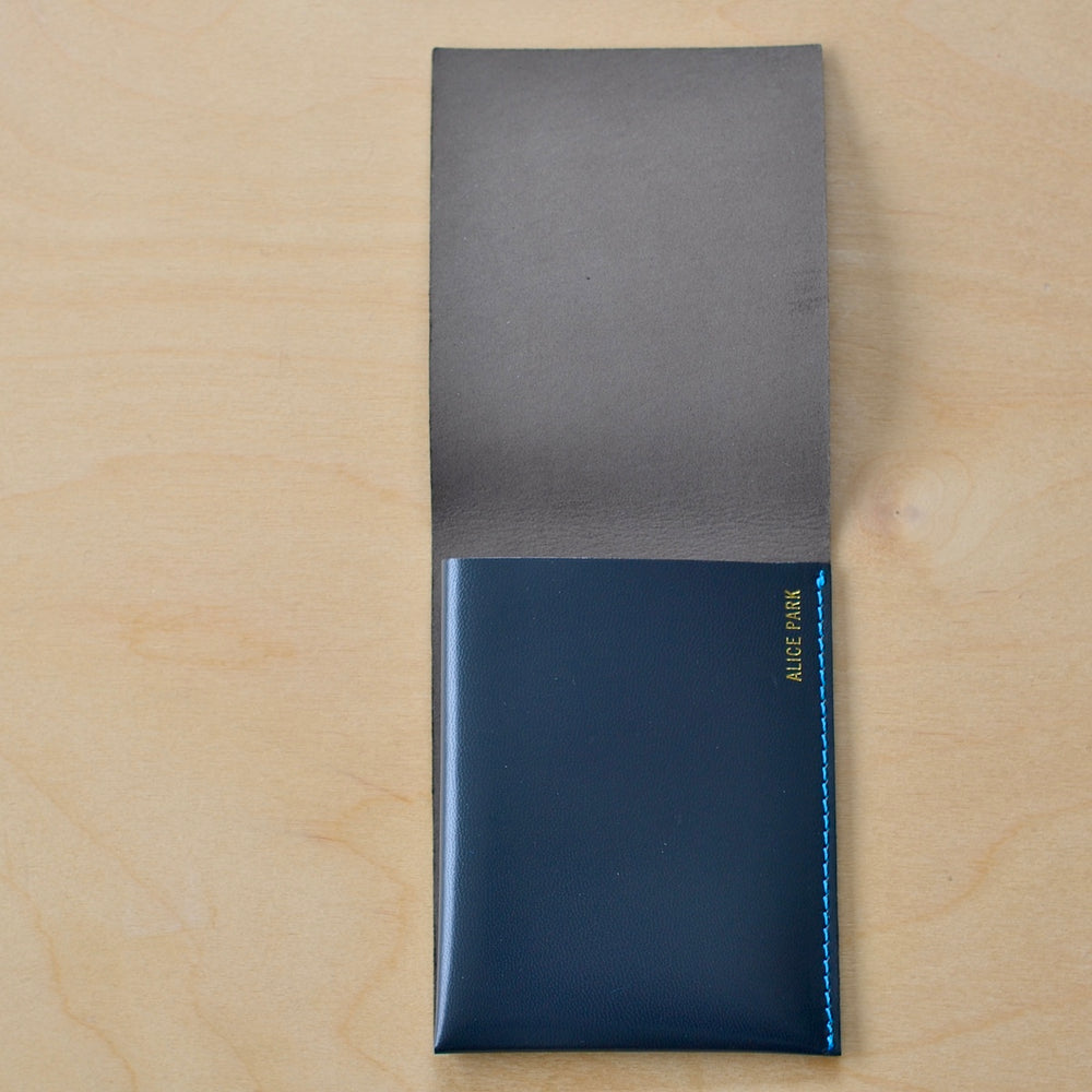 Simple Flap wallet in dark blue leather and blue stitching from architect Alice Park shown empty..