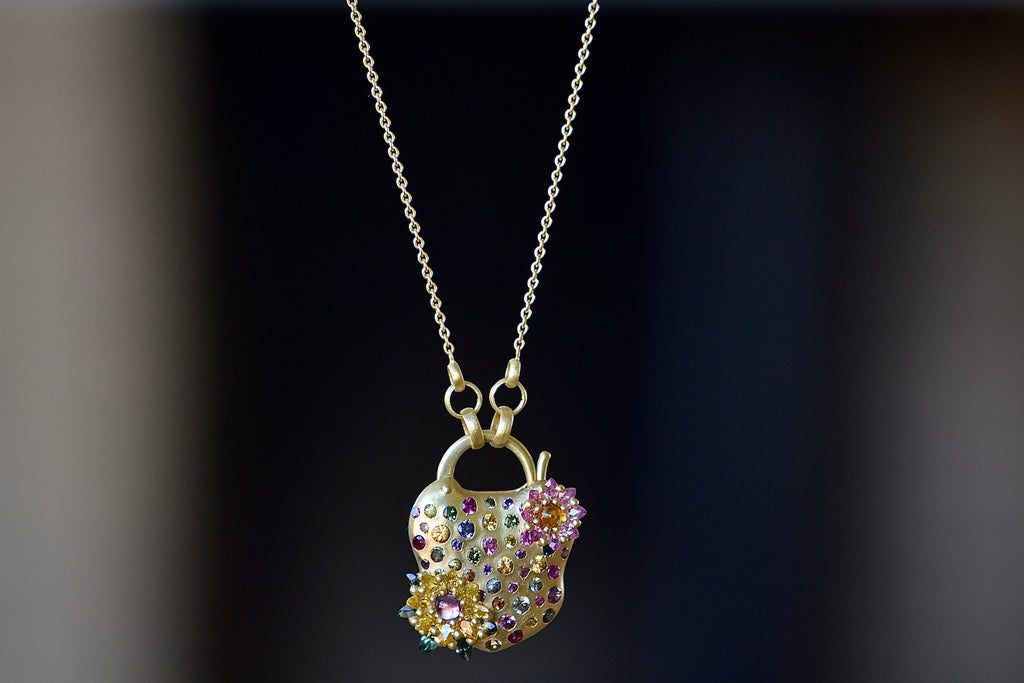 Double Daisy Cluster Padlock Necklace by Polly Wales is a medium padlock in yellow gold is scattered with rainbow sapphires in pink, green, yellow, lilac and orange and has two raised clusters of cabochon and brilliant sapphires in front and a confetti river on the back. It hangs on a beautiful chain that attaches to the lock handle by pulling the lever.  Recycled gold. Cast in Place. Cast not set. 