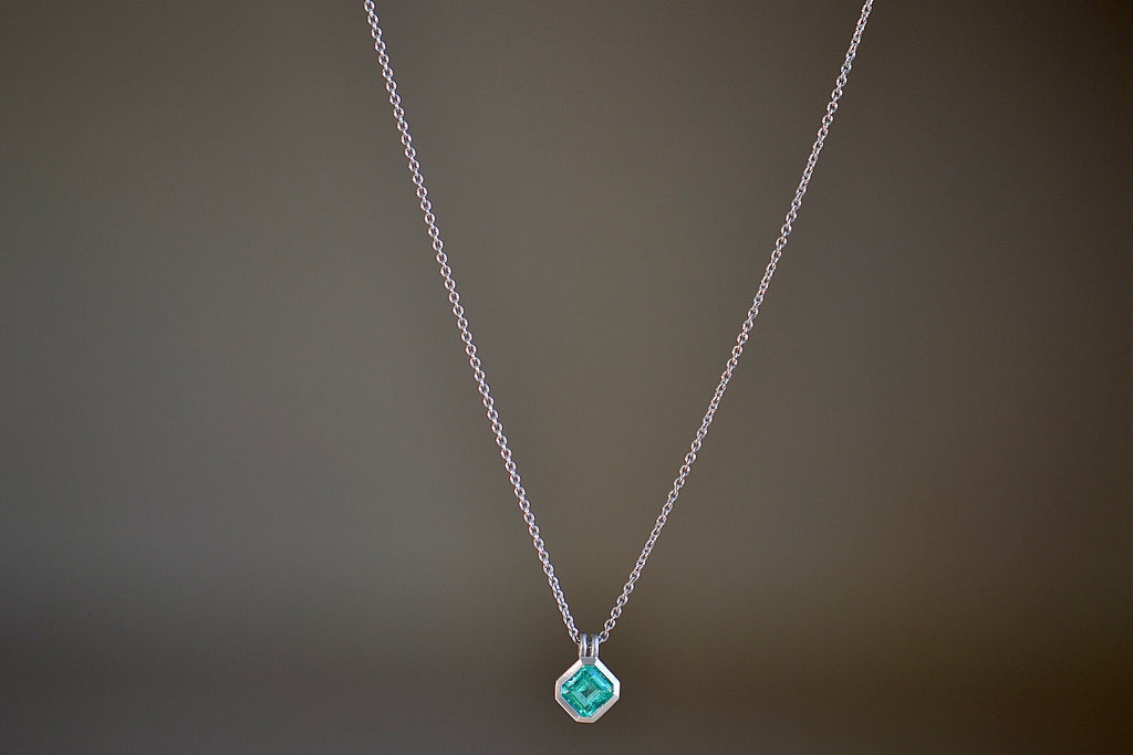 The duo bale emerald pendant in platinum by Elizabeth Street is a bezel set Colombian emerald set on its axis in a double bale and on a platinum chain.