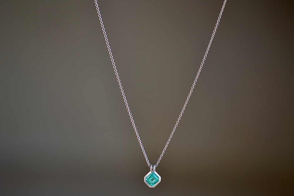 The duo bale emerald pendant in platinum by Elizabeth Street is a bezel set Colombian emerald set on its axis in a double bale and on a platinum chain.