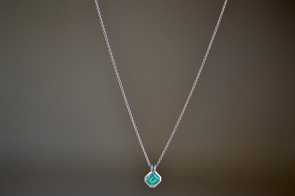 The duo bale emerald pendant in platinum by Elizabeth Street is a bezel set Colombian emerald set on its axis in a double bale and on a platinum chain.