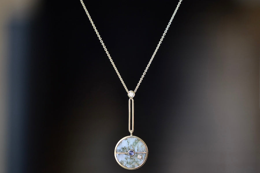  The signature Compass Pendant with Green Agate and Tanzanite by Retrouvai is a pendant necklace with stone inlay that is accented with a center gem stone and a white diamond. The compass hangs from an elongated paperclip link accented with a second white diamond on 24" 14k yellow gold chain.