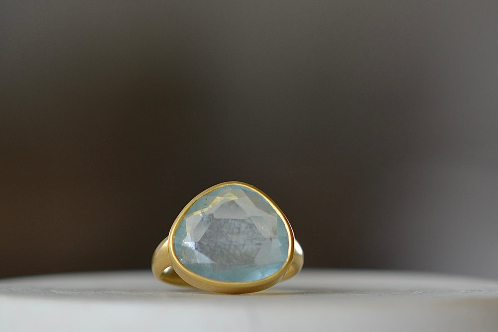The Aquamarine Large Greek ring, designed by Pippa Small Jewellery is an organically shaped and hand cut, faceted and translucent light blue aquamarine set in 18k yellow gold. Size 6 in stock.