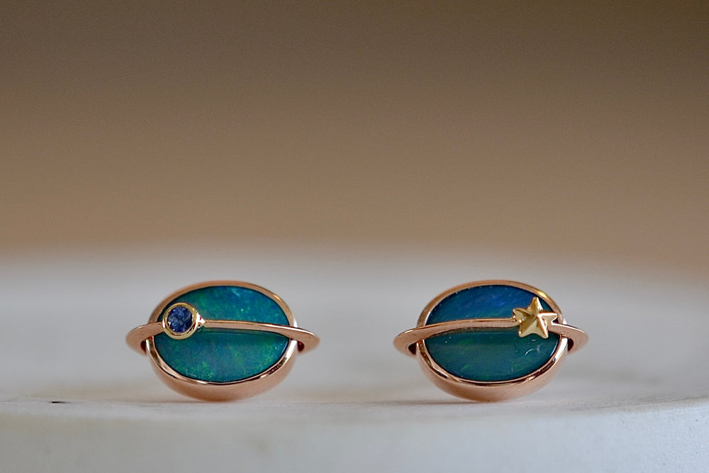 Small Planet Stud Earrings by Bibi Van Der Velden are comprised out of two bezel set opals with rings going through in rose gold of which one has a gold star and the other has a blue sapphire planet. 
