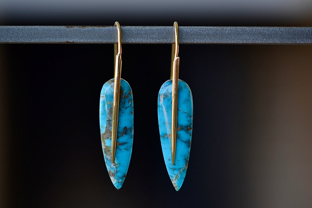 
            
                Load image into Gallery viewer, Feather Earrings in Turquoise by Rachela Atherley are One of a kind feather shaped slices of Turquoise hang on 18k yellow gold ear wire hooks that extend as a sword or spear and form these earrings.
            
        