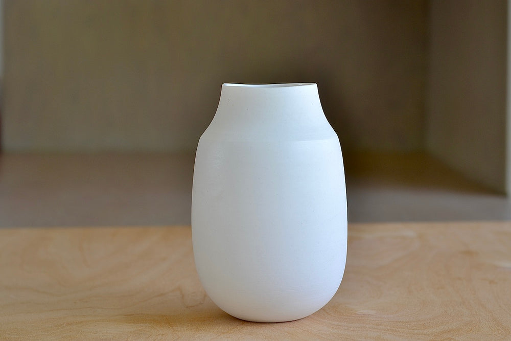 Lilith Rockett Vase with Neck "A" is Reminiscent of an eggshell, this vase is wheel thrown porcelain with gloss glaze on the interior and an unglazed exterior. It has been sanded smooth and it is very stable despite its rounded bottom. 