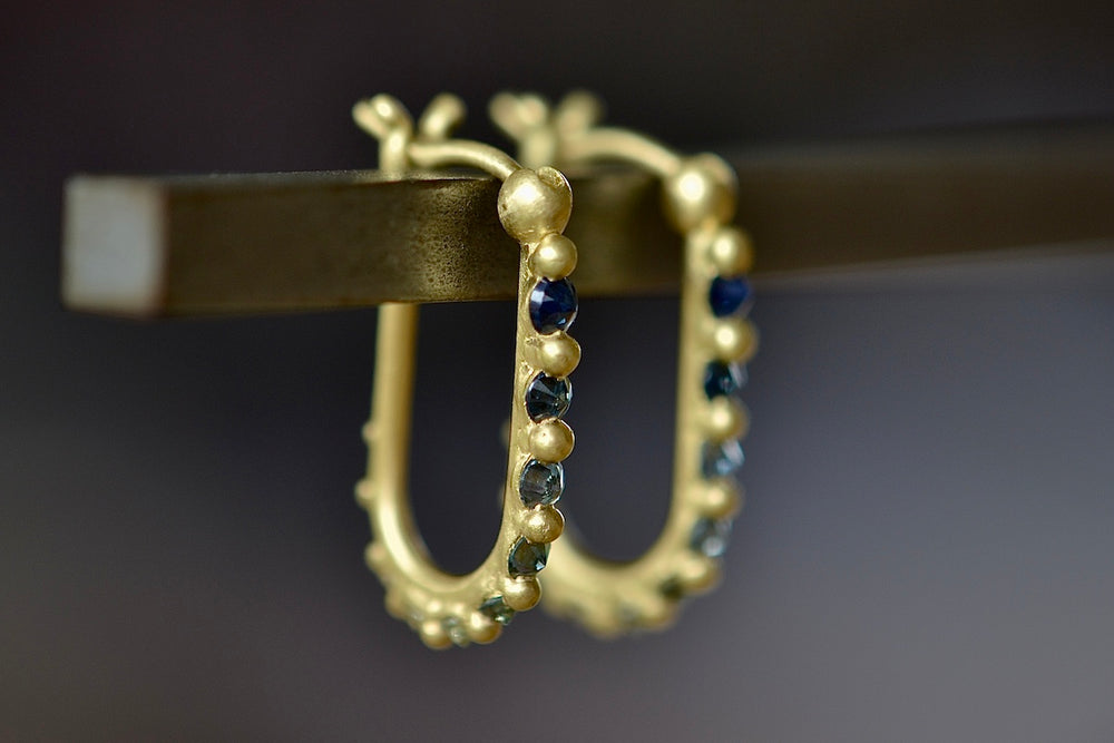 Oval Polaris U Hoop Earrings in Blue, green to yellow designed by Polly Wales is a hinge lock hoop in 18k gold that is encrusted with inverted and gradient blue to teal and green mixed sapphires with matte gold dots. Recycled gold. Handcrafted in Los Angeles.