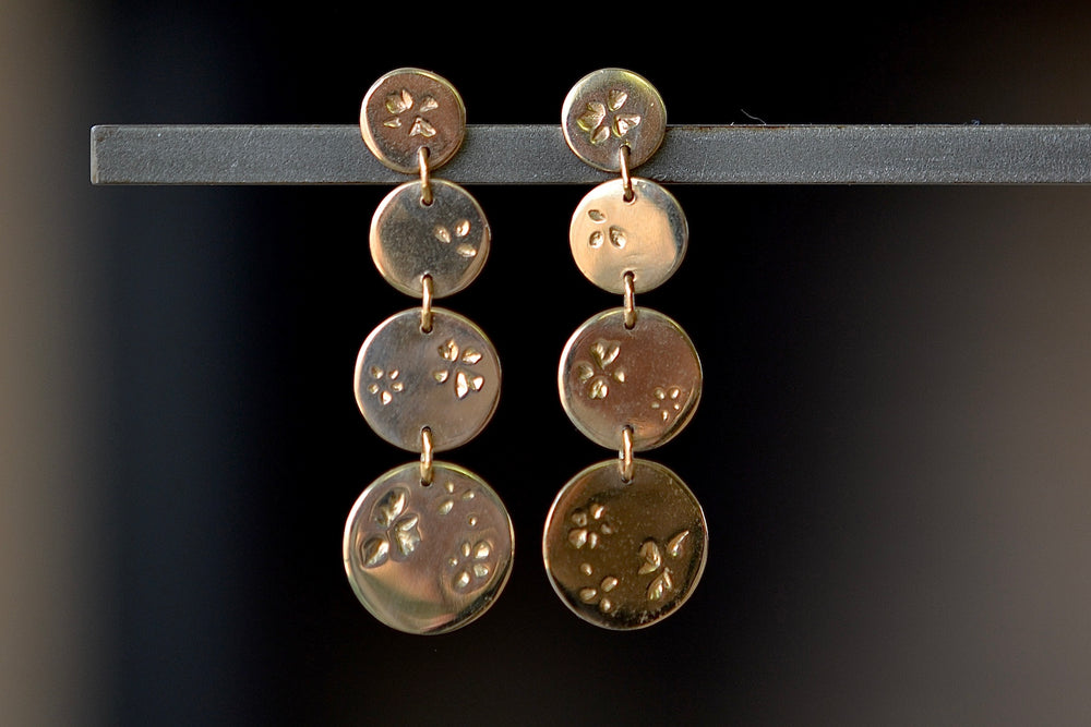 Falling Petal Dot Drops earrings by Kaylin Hertel are one each of graduated round discs from xs extra small, to small, medium and extra large on post closure in 14k yellow gold with her signature petal pattern.