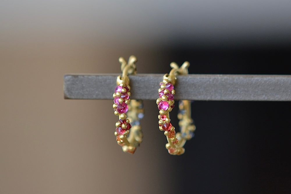 Polaris Vine Earrings in Rainbow Sapphires designed by Polly Wales are a small round hoop in 18k gold has an encrusted vine with inverted rainbow sapphires in yellow, pink, orange, green, blue and purple along with matte gold dots.