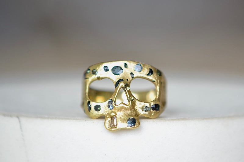 Stoned Mini Snaggle Tooth Skull ring by Polly Wales with green sapphires and a baguette diamond snaggle tooth.