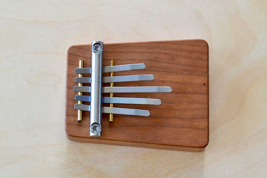 Side view of small kalimba with five (5) metal tines made in solid cherry wood in Germany.