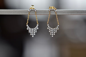 Alternate shot of Pétale Earrings by Yannis Sergakis are an arch of five bezel set and rhodium plated round cut diamonds with gold chains on each end hold together a cascade of twenty-five diamonds in a triangular shape to form a chandelier like earring on post closure in 18k gold. 