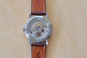 
            
                Load image into Gallery viewer, Close up of Back side of Weiss Watch 38mm Automatic Issue Field Watch with Navy Blue Dial and date, shown with dark brown Horween Leather strap. 
            
        