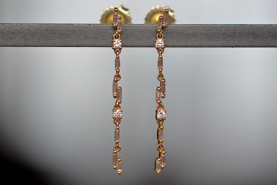 
            
                Load image into Gallery viewer, Alternate view of Linear Drop Earrings Designed by Suzanne Kalan are a sculptural combination of bezel set white baguette and round diamonds hang on a gold bar to form these dangle earrings with stud post closure. 
            
        