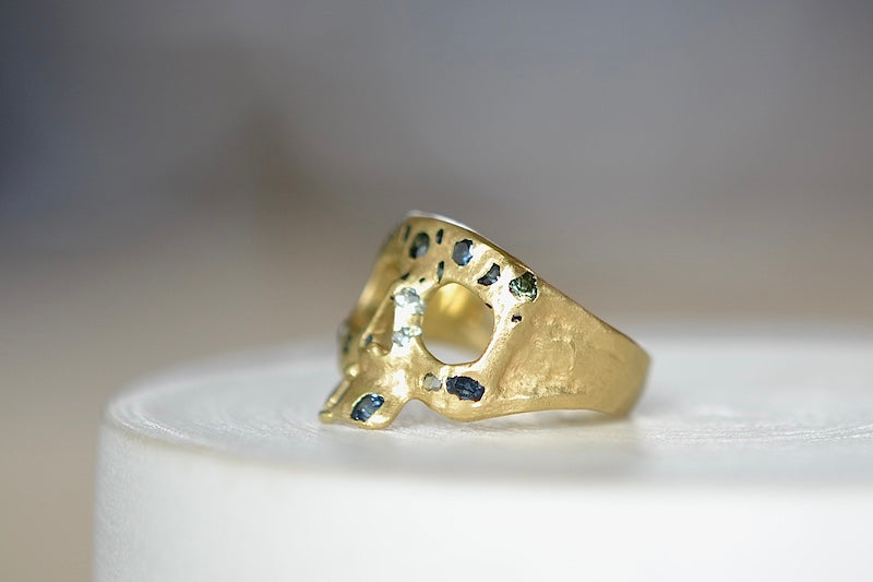 Side view of Stoned Mini Snaggle Tooth Skull ring by Polly Wales with green sapphires and a baguette diamond snaggle tooth.