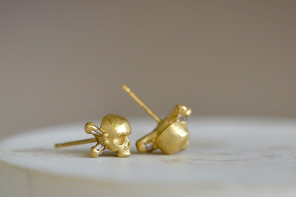 Side view of Polly Wales skull and bone stud earrings with diamond baguettes in 18k gold.