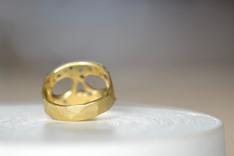 Back view of Stoned Mini Snaggle Tooth Skull ring by Polly Wales with green sapphires and a baguette diamond snaggle tooth.