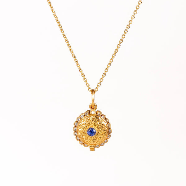 Mini Lace Locket by Arman Sarkisyan is a miniature scale locket in 22k gold with a blue sapphire center stone and lace like edging with white diamond accents hangs on a beautiful 18k gold chain. Detailed engraving on the back of locket which opens. Handmade in California.