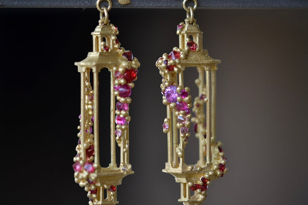 Close up detail of Polly Wales Jade Terrace Pagoda Earrings 18K yellow recycled gold pagoda forms hanging from a bird stud encrusted with a pearl pink and orange sapphire sapphires. Cast not set.