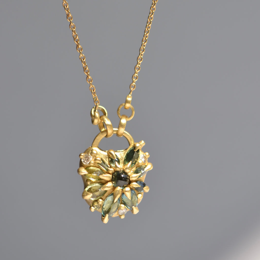 Green Fantaisie Encrusted Padlock Necklace by Polly Wales is a padlock in 18K yellow gold and encrusted with mixed green sapphires, a center cabochon and an accent diamond hanging on a chain that attaches to the lock handle by pulling the lever. Recycled gold. Cast in Place. Cast not set. 