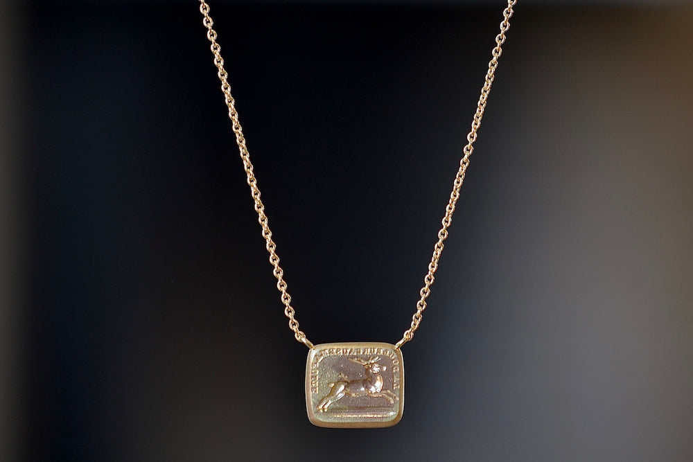 Pain Makes Me Fly Duo Motto Necklace by Makiko Wakita made  by stamping an 1800s carved seal with 'mottos' in French, Italian, Latin or English on to gold. A rectangular disc in gold with satin finish that will turn shiny over time features an image of a running stag/hart/deer pierced by an arrow with French words "La Douleur Cause Ma Fuite" (‘Pain Makes Me Fly’ or ‘Pain and Sorrows Cause Me To Flee’). This piece could signify a loss in love or life, but not in pride and spirit, and endure and move for