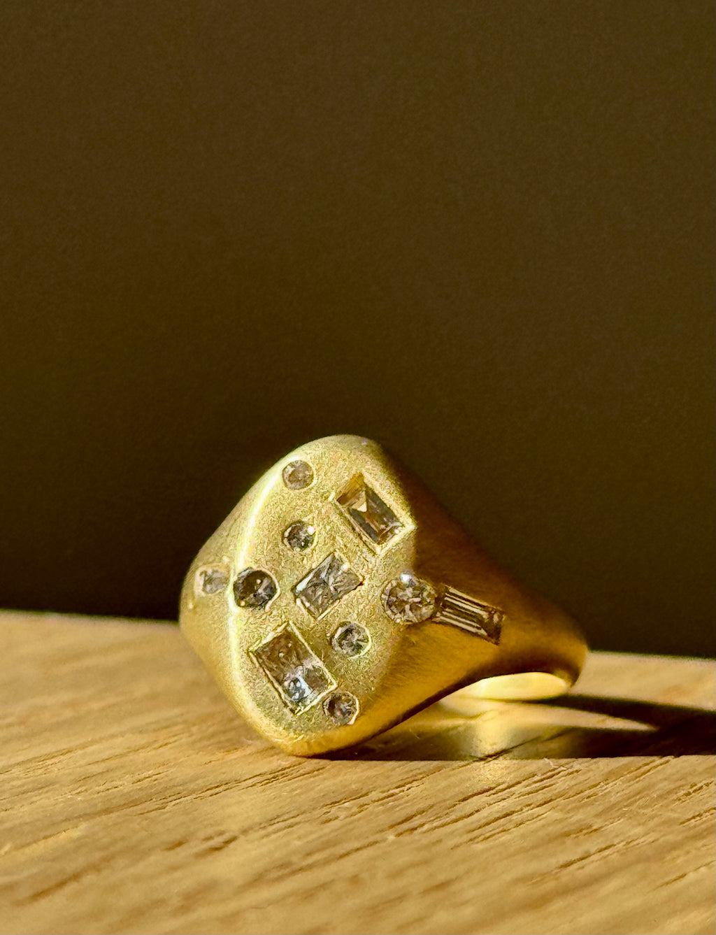 This image features a distinctive and luxurious Diamond Confetti Signet Ring by Polly Wales. Crafted in 18-karat gold, the ring showcases a classic signet design adorned with a mix of round and baguette cut white diamonds, creating a stunning contrast against the golden metal.