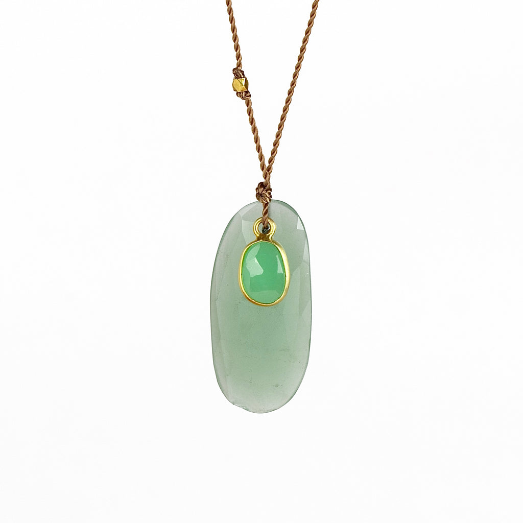 Close up of Chrysoprase and Sapphire necklace, a one of a kind lightly faceted Chrysoprase stone slice accompanied by a smaller green and faceted sapphire slice of which the smaller is set in 18k gold with with a gold bead on the string makes this one of a kind &nbsp;organic pendant necklace. Designed by Margaret Solow. Handcrafted in Los Angeles.