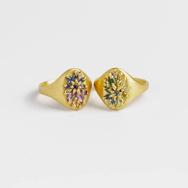 Encrusted Lotus signet rings by Polly wales are  oval set signet rings in 18k polished gold with encrusted mixed cut sapphires and white diamonds in two color ways. on white background.