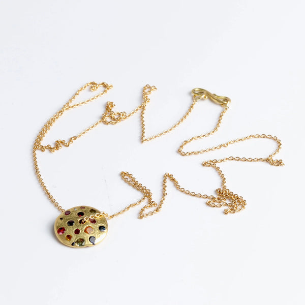 Polly Wales Spinning Disc Pendant Necklace in 18K yellow gold with scattered rainbow sapphires in orange, yellow, pink, blue, purple and lilac hangs on a beautiful chain 22" cast in place and cast not set in recycled gold on white background.