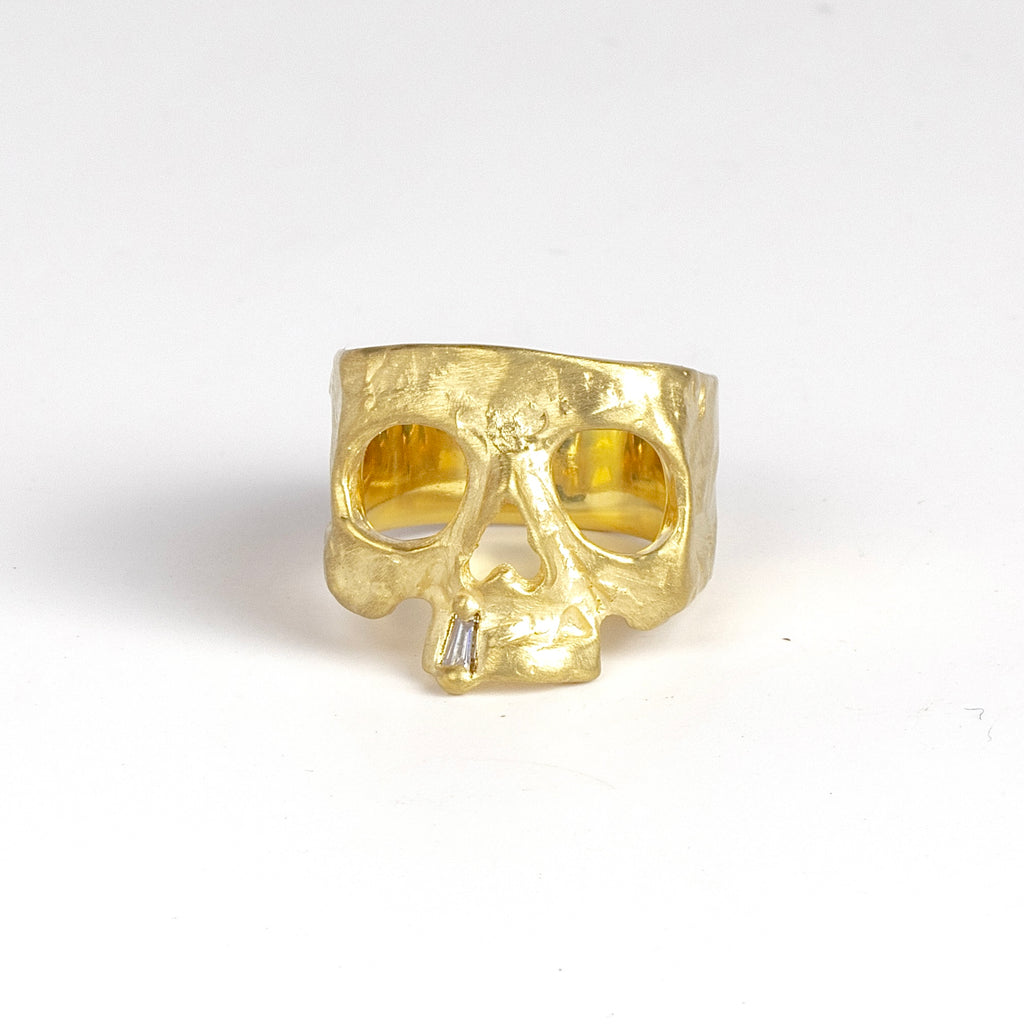 Snaggle Tooth Skull ring by Polly Wales on white is an 18k gold squared skull ring with a white diamond baguette snaggle tooth. Available in size 7 and 7.5 at OK store, Los Angeles.