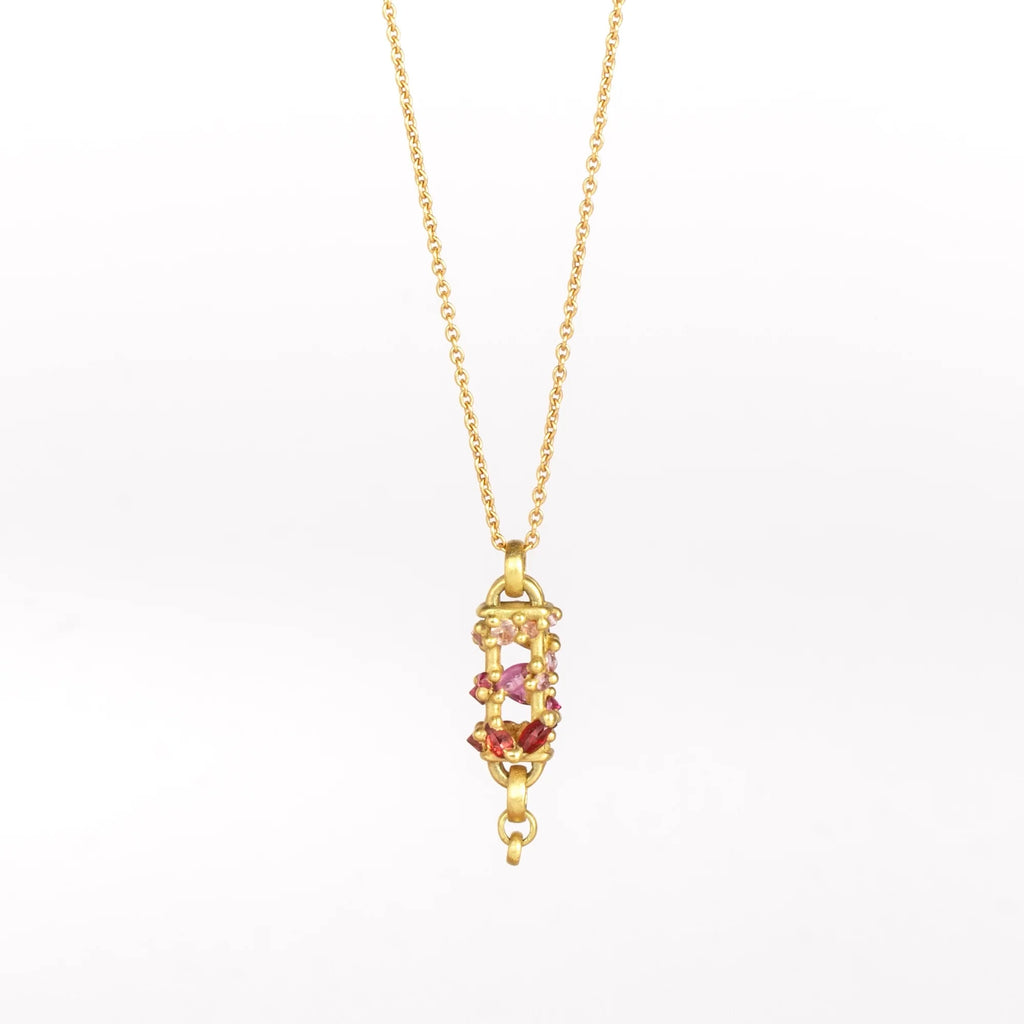 Vertical Fontaine Bar Necklace in Plum Blossom by Polly Wales is an oval and three dimensional bar in 18K yellow gold holds a vine of encrusted and inverted sapphires in pink, fuchsia and red that have been cast and are accompanied by matte gold dots. The bar hangs on a beautiful gold chain and bale. Shown on white background.