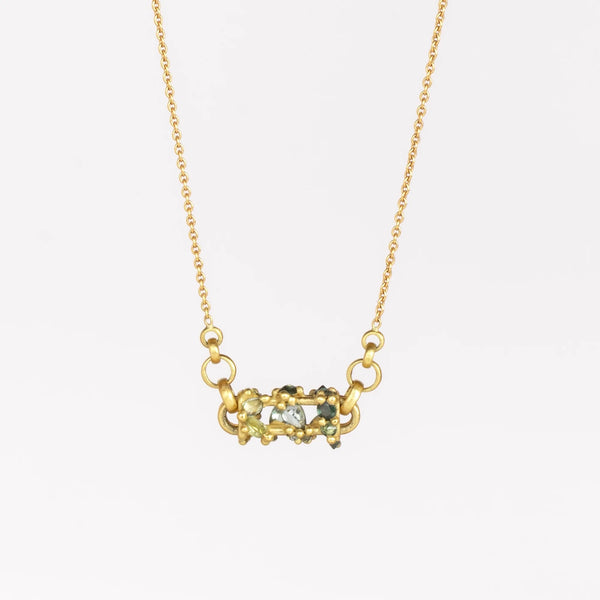 Horizontal Fontaine Bar Necklace in Green by Polly Wales shown on white background. This is an oval bar in 18K yellow gold has a vine of encrusted inverted sapphires in green, gray and black that have been cast and are accompanied by matte gold dots. The bar hangs on a beautiful gold chain. Recycled Gold. Handmade in Los Angeles. Cast not set.