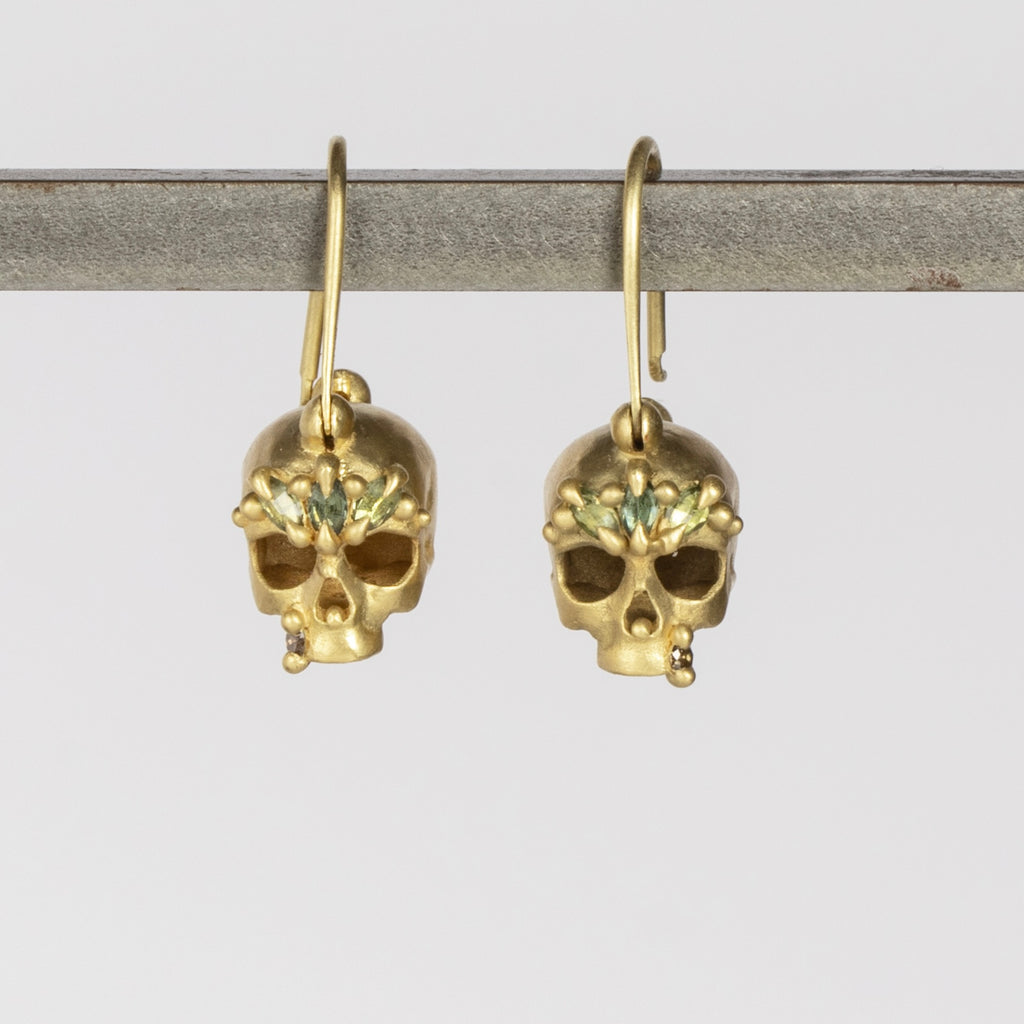Green Enchanted Skull Safety Pin Earrings by Polly Wales are a pair of safety pin earrings in 18k gold with skulls that have been encrusted with green sapphires and diamonds. Recycled gold. Handcrafted in Los Angeles