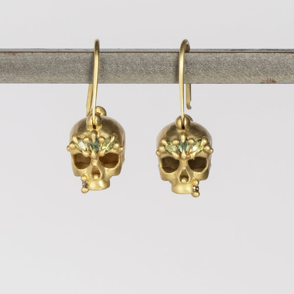 Green Enchanted Skull Safety Pin Earrings by Polly Wales are a pair of safety pin earrings in 18k gold with skulls that have been encrusted with green sapphires and diamonds. Recycled gold. Handcrafted in Los Angeles