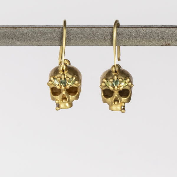 Green Enchanted Skull Safety Pin Earrings by Polly Wales are a pair of safety pin earrings in 18k gold with skulls that have been encrusted with green sapphires and diamonds. Recycled gold. Handcrafted in Los Angeles