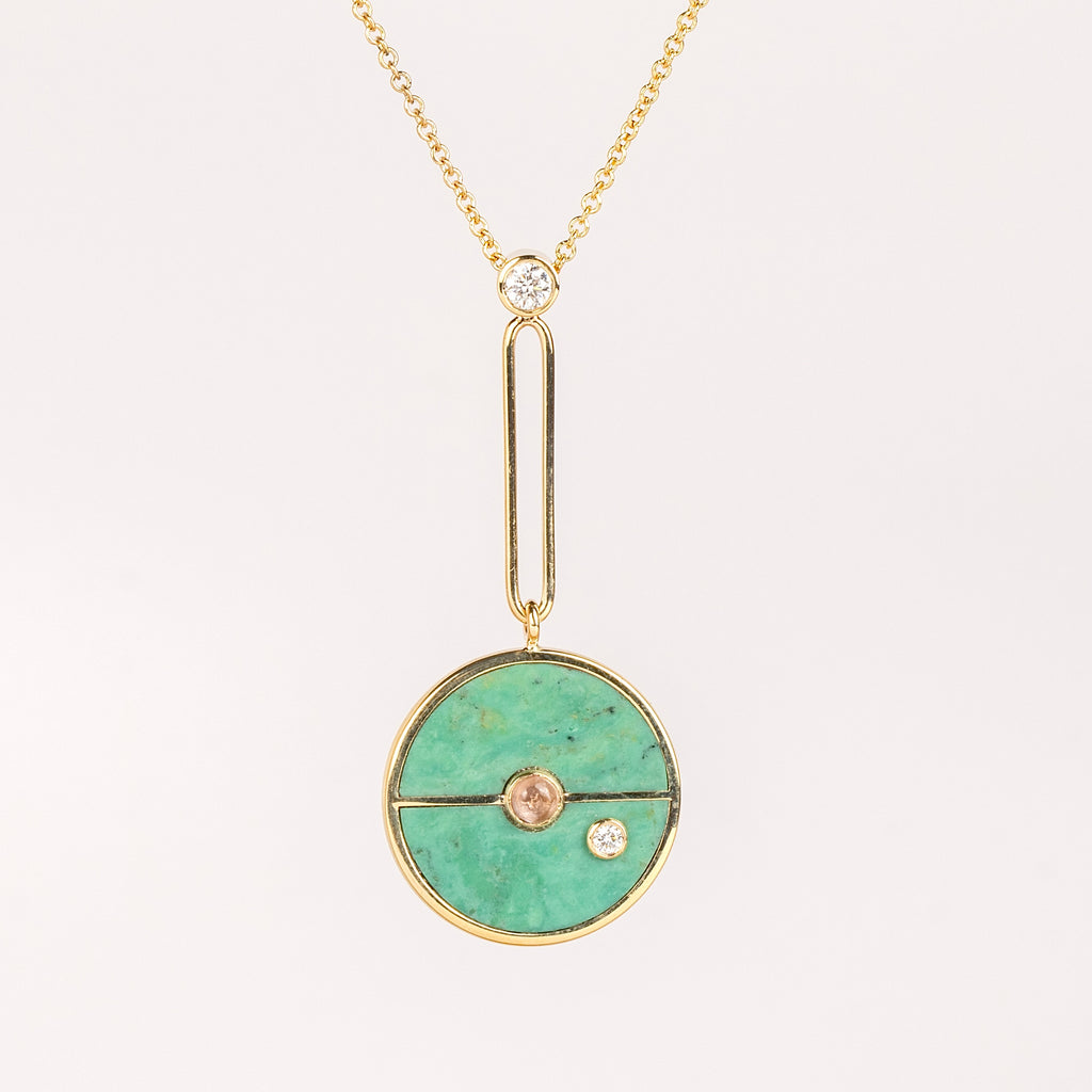 Compass Pendant in Green Turquoise and Lotus Garnet by Retrouvai is a unique modern take on an heirloom pendant. Stone inlay is accented with a center gem stone and white diamond. The compass hangs from an elongated paperclip link accented with a second white diamond. Handcrafted in Los Angeles.