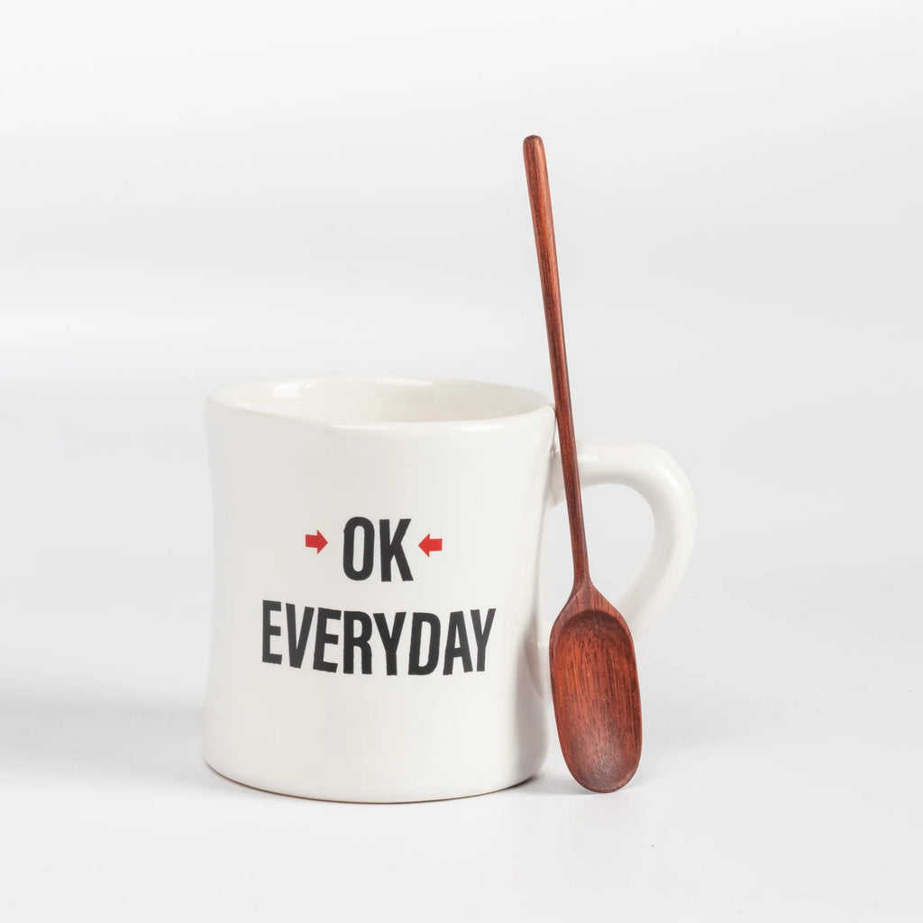 Single hand carved wood spoon leaning against OK mug.