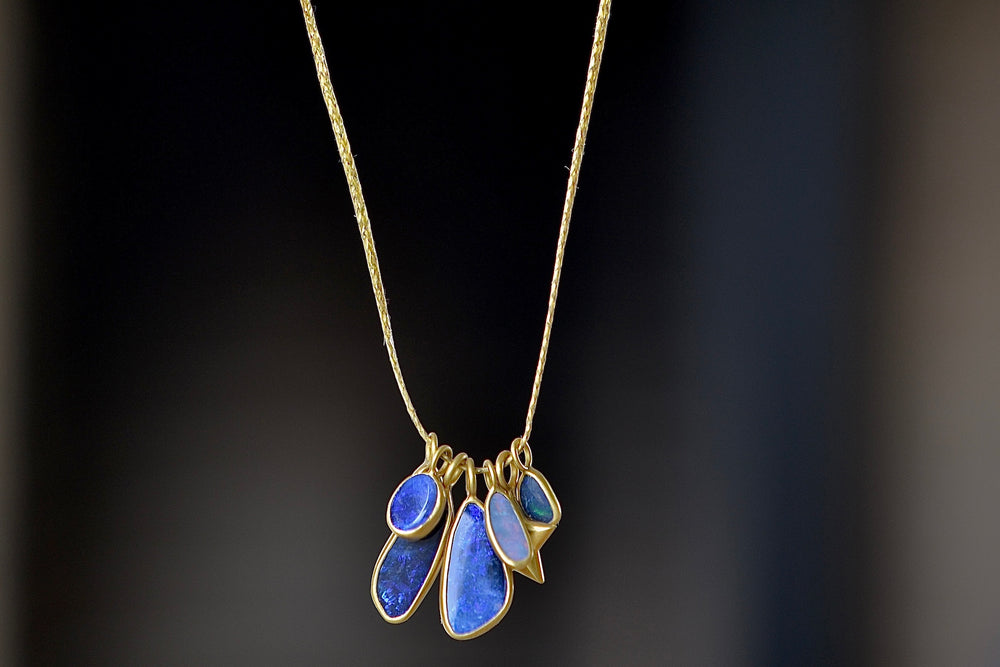 The Colette Opal Cluster Necklace is a cluster of six various sized and bezel set boulder opals in the Caribbean dreams color-way, accompanied by a gold star and hanging on a 18" golden waxed cotton cord.